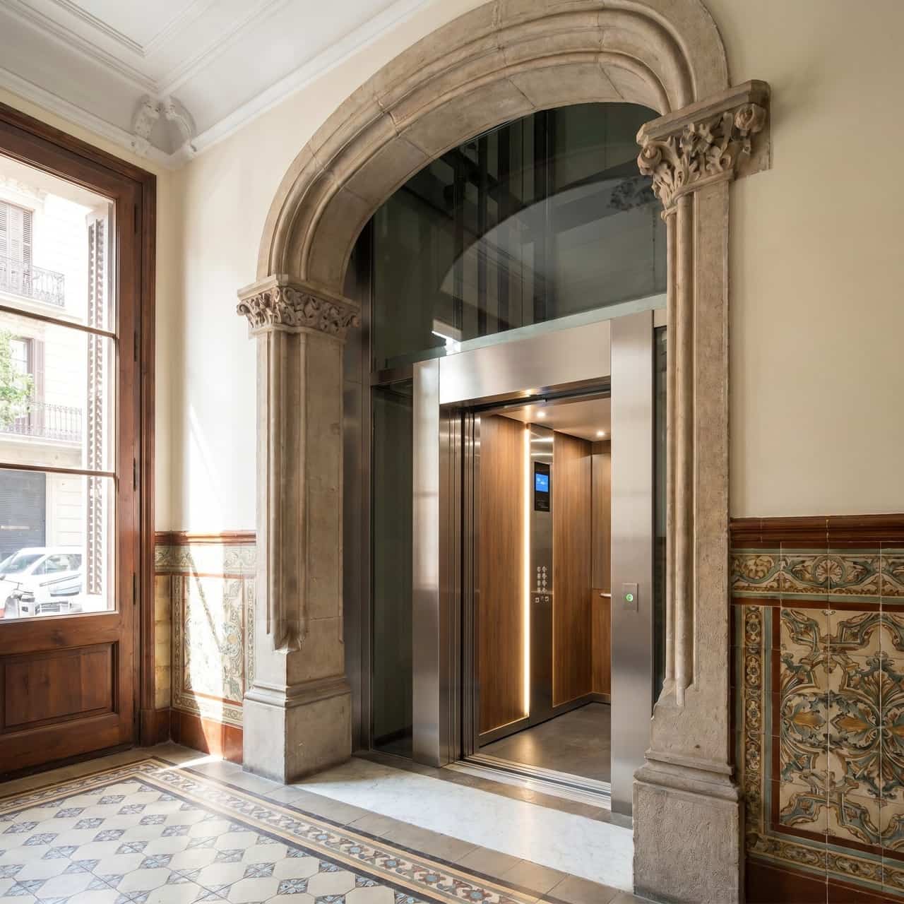 Escalera de comunidad de propietarios antigua en Barcelona con ascensor nuevo de cristal y acero integrado en el hueco