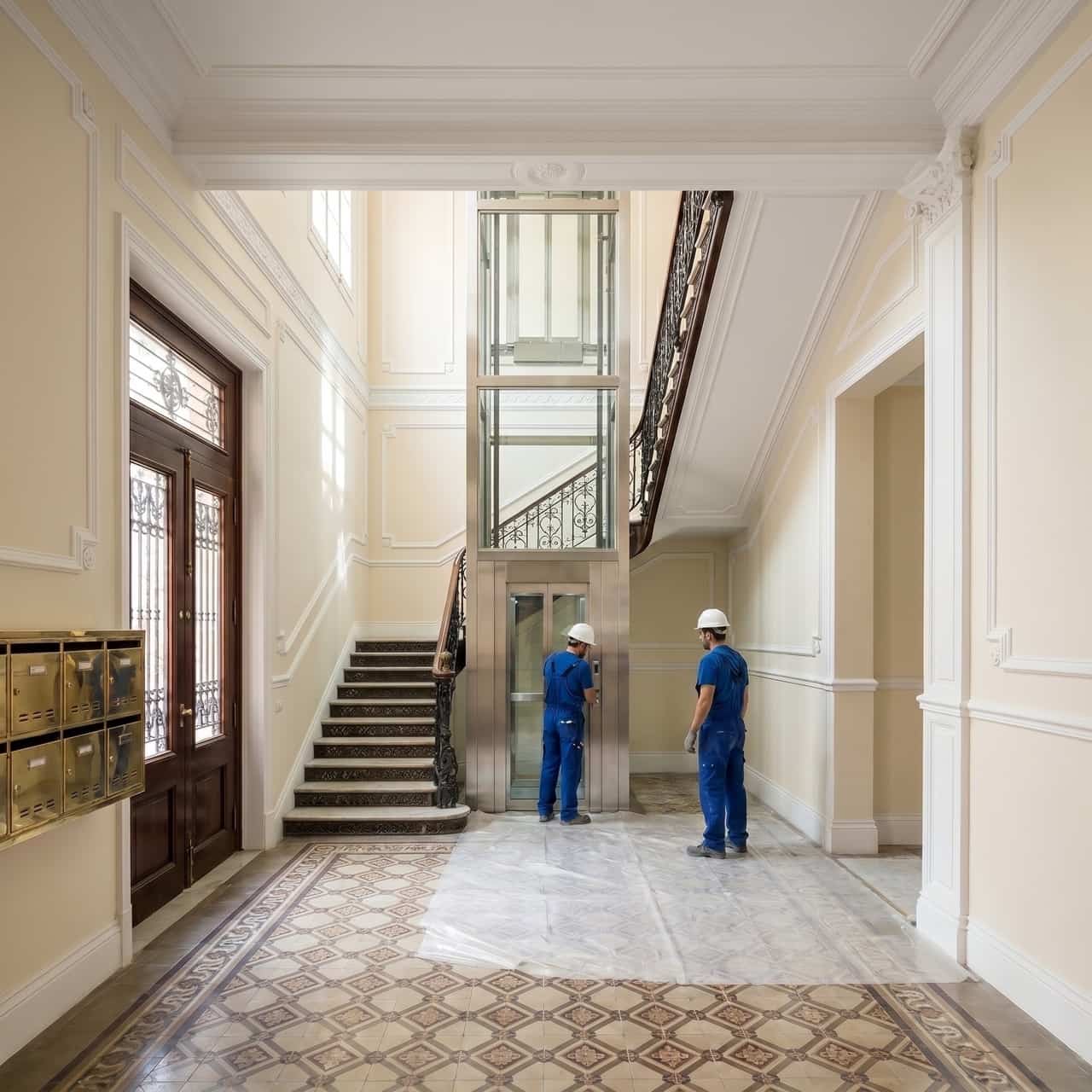 Ascensor nuevo de cristal y acero instalado en el hueco de escalera de una finca antigua de Barcelona